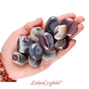 May include: A collection of agate stones in various shades of gray, brown, and purple. The stones are smooth and polished, with intricate patterns of banding and swirls.