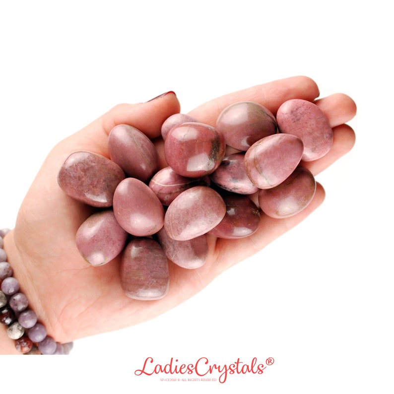 May include: A collection of smooth, polished rhodonite stones in various shades of dusty pink and muted rose, featuring natural dark veining and inclusions. The stones are rounded and oval in shape, displaying a glossy, reflective surface texture.