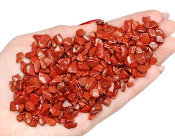 May include: A handful of polished, red jasper stones. The stones are small, irregularly shaped, and vary in shades of red. The image includes the text "Ladies Crystals" in a cursive font.