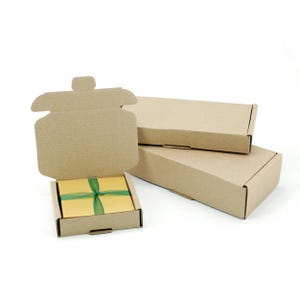 Op de afbeelding: Drie kartonnen dozen, &eacute;&eacute;n open met een klein cadeaudoosje erin. Het cadeaudoosje is ingepakt in geel papier met een groen lint. De dozen zijn allemaal bruin en gemaakt van golfkarton.