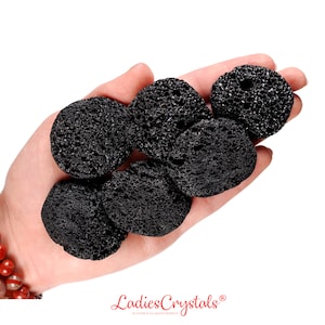 May include: A hand holding six black lava rock stones. The stones are round and have a rough, porous texture.
