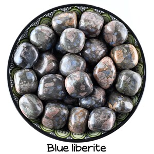 Könnte beinhalten: Eine Schale gefüllt mit blauen Liberit-Trommelsteinen. Die Steine sind eine Mischung aus Grau, Blau und Rosa mit einem gefleckten Muster. Die Schale hat ein grünes und schwarzes Muster.