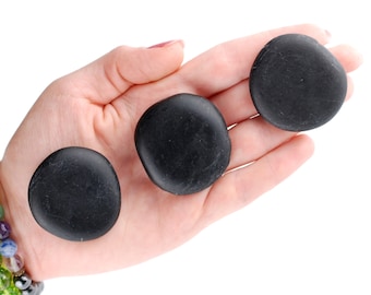May include: Three smooth, black, round stones in a person's hand. The stones are approximately the same size and shape.
