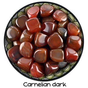 Może przedstawiać: Miska wypełniona gładkimi, polerowanymi kamieniami z ciemnoczerwonego karneolu. Kamienie mają głęboki, bogaty kolor.