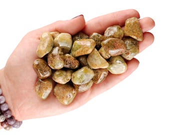 May include: A hand holding a pile of green garnet tumbled stones. Green garnet is a type of gemstone.
