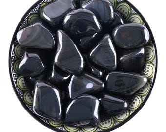 May include: A bowl of black obsidian rainbow tumbled stones. The stones are smooth and polished, with a rainbow sheen.