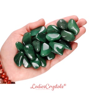May include: A hand holding a pile of smooth, green aventurine tumbled stones. The stones are various sizes and shapes, with a glossy finish.