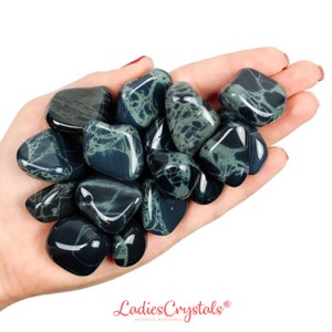 Puede incluir: Una mano sosteniendo un montón de piedras pulidas de color negro y verde. Las piedras tienen un patrón veteado único.