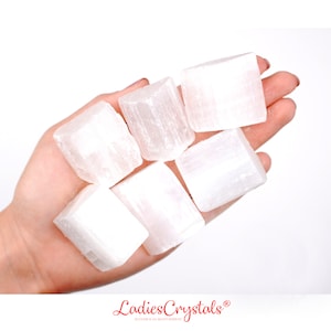 May include: Six white selenite crystal cubes in a hand. The crystals are smooth and have a striated texture.