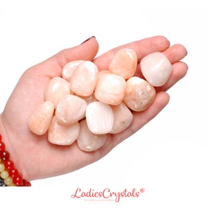 May include: A collection of smooth, pale pink and white tumbled stones. The stones are in a person's hand, and they have a slightly iridescent sheen.