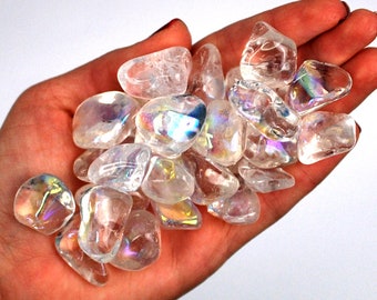 May include: A collection of iridescent clear quartz tumbled stones. The stones are smooth and have a rainbow sheen.