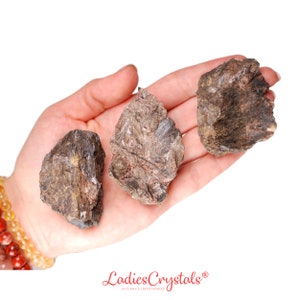 May include: Three rough, brown and gray, irregularly shaped, natural stones. The stones are in the palm of a hand.