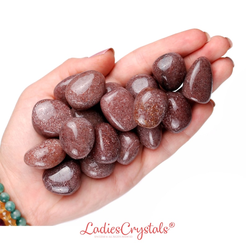 May include: A pile of tumbled red jasper stones in a hand. The stones are smooth and have a speckled appearance.