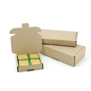 May include: Cardboard shipping boxes, one open to reveal a gold box tied with a green ribbon. Two additional closed boxes are stacked behind the open box. The boxes are made of corrugated cardboard and are on a white background.