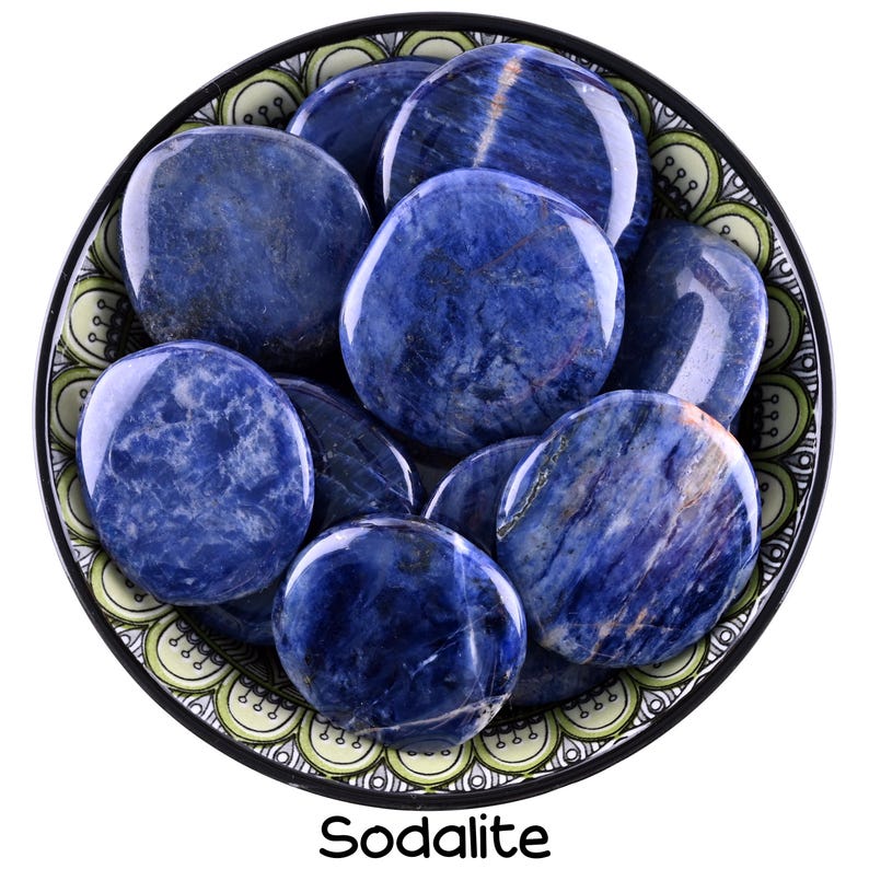 Puede incluir: Un cuenco de piedras de sodalita lisas y pulidas. Las piedras son de un azul profundo con vetas blancas y est&aacute;n dispuestas en un patr&oacute;n circular. El cuenco est&aacute; decorado con un patr&oacute;n verde y blanco.