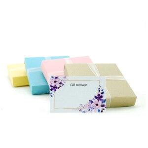 May include: Four gift boxes in yellow, light blue, pink, and brown with a white ribbon. A white card with a floral design and the text "Gift message" is in front of the boxes.