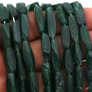 May include: A strand of dark green faceted glass beads. The beads are long and narrow, with a slightly rounded shape. They are strung on a clear thread.