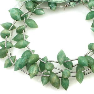 Könnte beinhalten: Stränge grüner Edelsteinperlen in Blattform. Die Perlen sind auf silberfarbenem Draht aufgefädelt, wodurch eine halskettenartige Anordnung entsteht. Die Edelsteine haben eine facettierte Oberfläche. Der Hintergrund ist weiß.