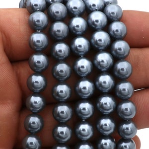 Op de afbeelding: Strengen grijze parel kralen. De kralen zijn rond en hebben een glanzende afwerking. De kralen zijn aan elkaar geregen, waardoor een ketting of armband ontstaat. De kralen hebben een koele grijze kleur.