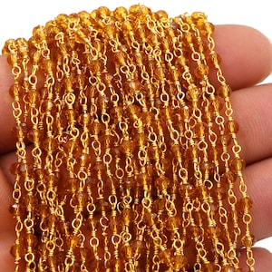 Könnte beinhalten: Nahaufnahme einer Kette aus goldfarbenen Perlen. Die Kette besteht aus kleinen, facettierten Perlen, die mit goldfarbenem Draht aufgereiht sind. Die Perlen haben einen warmen, bernsteinfarbenen Farbton, und der Draht hat eine helle, glänzende Oberfläche. Die Kette wird wahrscheinlich zur Schmuckherstellung verwendet.