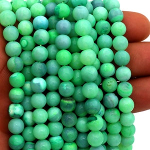 Peut inclure: Un fil de perles rondes et polies dans des tons de vert, du clair à l'émeraude profond. Les perles sont tenues dans une main, mettant en valeur leur texture lisse et leurs variations de couleur. Les perles mesurent environ 8 mm de diamètre.