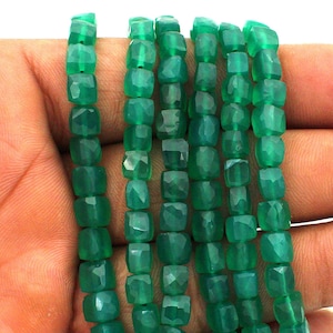 Può includere: Una fila di perline di pietra preziosa verde, di forma quadrata e sfaccettate. Le perline sono traslucide con una finitura lucida e sono infilate in una linea continua, mostrando una tonalità verde smeraldo uniforme lungo tutta la fila.