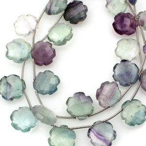 Può includere: Una collana di perline di fluorite sfaccettate di colore verde, viola e trasparente a forma di fiore. Le perline sono infilate su un filo d'argento.