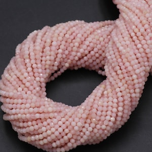 Puede incluir: Un conjunto de pequeñas cuentas redondas de color rosa claro. Las cuentas están ensartadas juntas, formando una masa densa y texturizada. Las cuentas son de un color rosa pastel suave, y el efecto general es delicado y femenino. Las cuentas son probablemente para la fabricación de joyas.