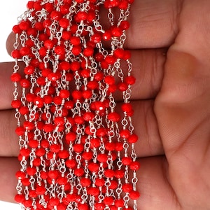 Op de afbeelding: Een streng rode facetgeslepen kralen geregen aan een zilveren ketting. De kralen zijn klein en rond, en de ketting is delicaat.