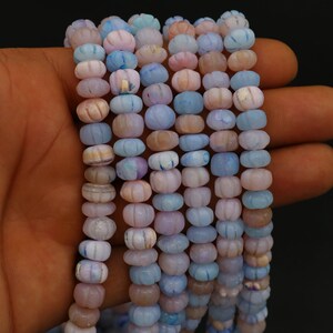 Op de afbeelding: Strengen pastelkleurige kralen in tinten blauw, roze en lavendel. De kralen hebben een unieke pompoenvorm en zijn aan elkaar geregen. De kralen worden in een hand tegen een donkere achtergrond gehouden.
