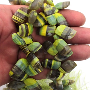 May include: A collection of faceted gemstone beads in shades of yellow, green, and brown. The beads have a striped pattern and are strung together. The beads are held in a hand.