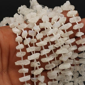 May include: A strand of white rainbow moonstone beads, each bead is a rough, irregular shape and has a silvery sheen.