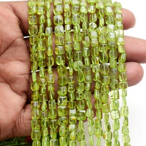 Può includere: Un cartello in legno rustico con la scritta "Welcome" in stile scritto a mano. Il cartello è dipinto di bianco con una finitura invecchiata e presenta un elemento floreale decorativo nell'angolo. Lo sfondo è un'immagine sfocata di una superficie in legno.