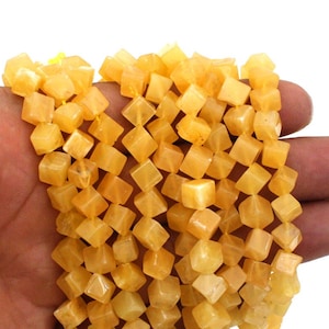 May include: A strand of yellow gemstone beads, each bead is faceted and shaped like a cube. The beads are strung on a clear thread.