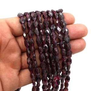 May include: A strand of dark red faceted gemstone beads. The beads are oval shaped and have a glossy finish.