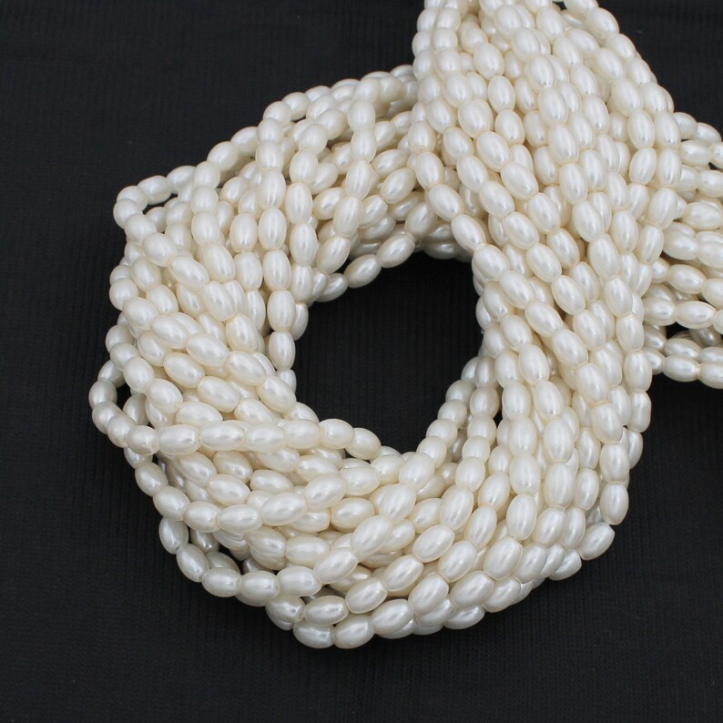 May include: A strand of white oval-shaped plastic beads. The beads are strung together on a clear thread.