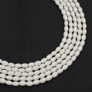 May include: A strand of white oval-shaped faux pearl beads. The beads are strung on a clear thread and are arranged in a circular pattern.