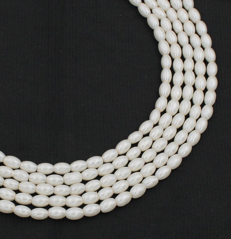 May include: A strand of white oval-shaped faux pearl beads. The beads are strung on a clear thread and are arranged in a circular pattern.