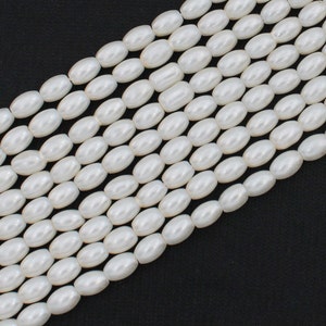 May include: A strand of white oval-shaped beads. The beads are smooth and have a pearlescent finish.