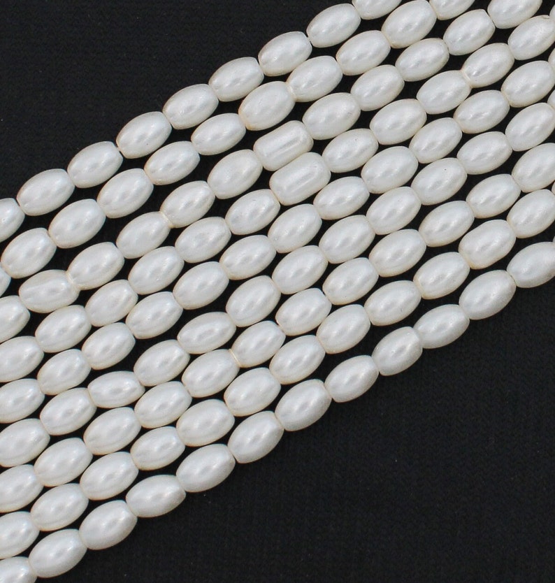 May include: A strand of white oval-shaped beads. The beads are smooth and have a pearlescent finish.