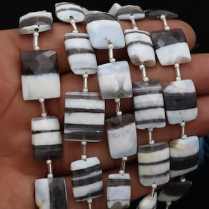 Può includere: Una collana di perle di opale con bande nere e bianche. Le perle sono rettangolari e hanno una finitura lucida. Le perle sono infilate su un filo d'argento.