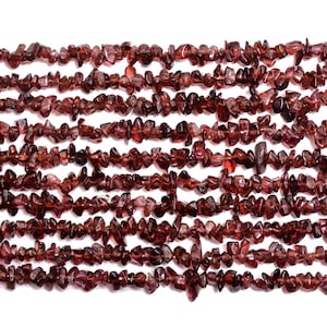 Può includere: Un filo di perline di granato rosso a forma di chip. Le perline sono piccole e di forma irregolare, e hanno una finitura naturale non lucidata.