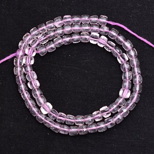 Può includere: Una collana di perline di pietra preziosa sfaccettata rosa pallido. Le perline sono di forma quadrata e hanno un aspetto traslucido.