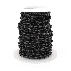 May include: A spool of black faceted glass beads strung on a silver chain. The beads are small and uniform in size. The chain is delicate and has a subtle shine.