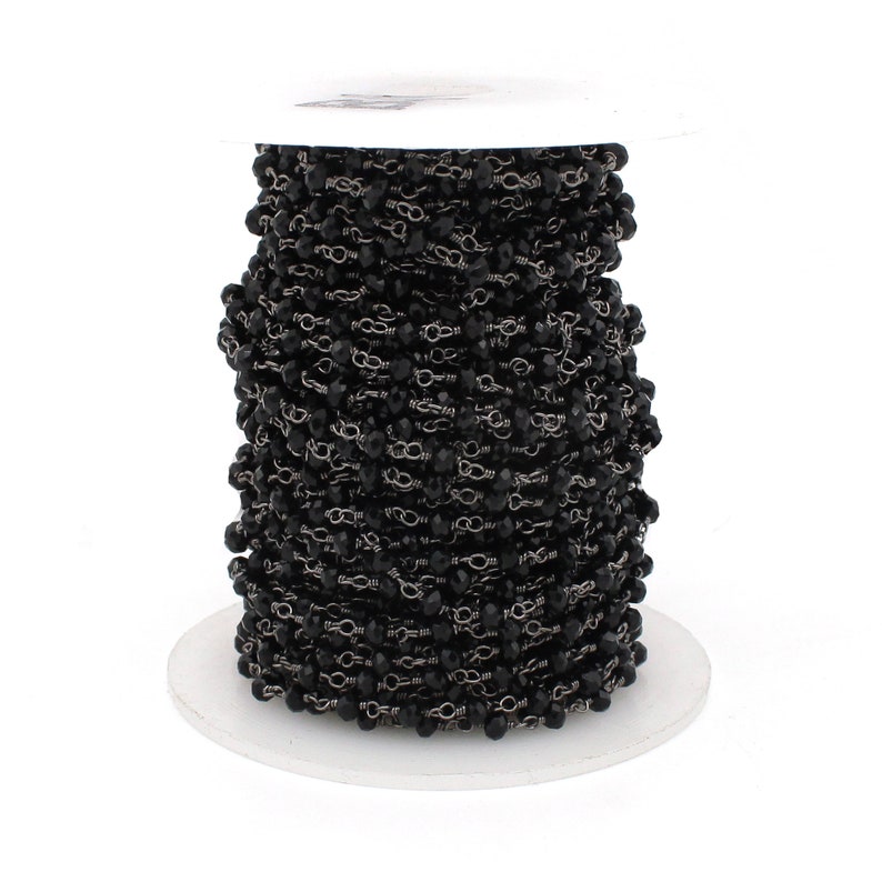 May include: A spool of black faceted glass beads strung on a silver chain. The beads are small and uniform in size. The chain is delicate and has a subtle shine.
