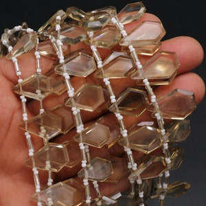 Puede incluir: Una hebra de cuentas de piedra preciosa facetadas de color marr&oacute;n claro con un patr&oacute;n de cuentas espaciadoras plateadas y blancas.