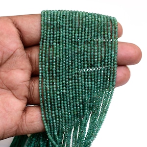 Peut inclure: Un long collier de petites perles rondes et facettées de couleur verte. Les perles sont de taille uniforme et présentent une teinte vert forêt profond avec des variations naturelles de ton et de texture, disposées en plusieurs rangées verticales.