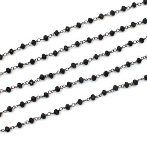 May include: Black beaded chain with a silver finish. The chain is made of small, round beads and is strung on a thin, silver chain.