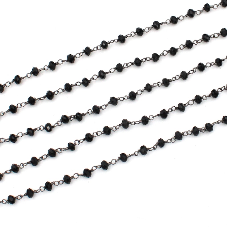 May include: Black beaded chain with a silver finish. The chain is made of small, round beads and is strung on a thin, silver chain.