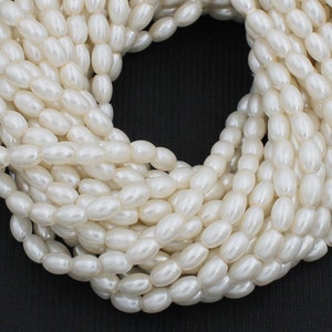May include: A strand of white oval-shaped beads. The beads are smooth and have a pearlescent finish.